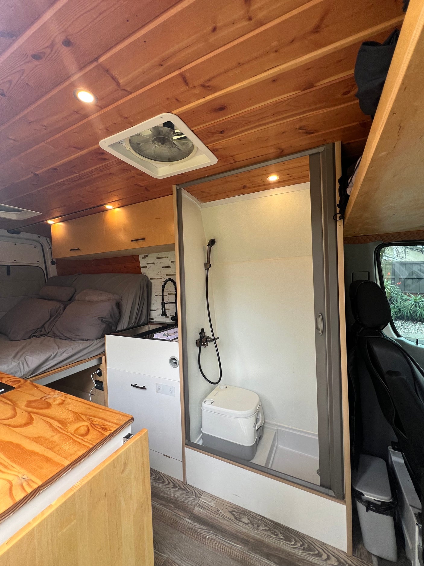Cozy RV rental interior with wooden ceiling, functional shower, toilet, bed, and kitchen. Ideal for compact travel.