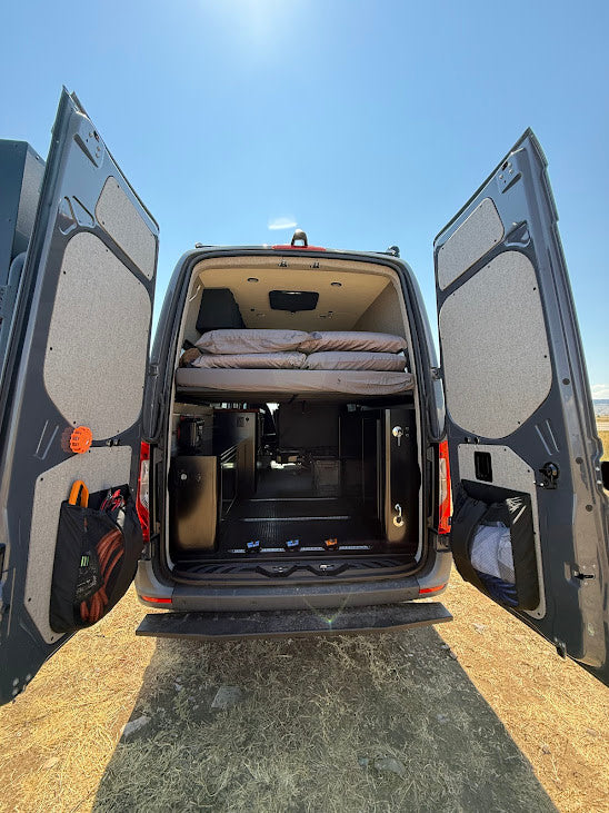 Rear view of a camper van with open doors, revealing a raised bed & custom interior storage. Ideal for RV rental road trips.