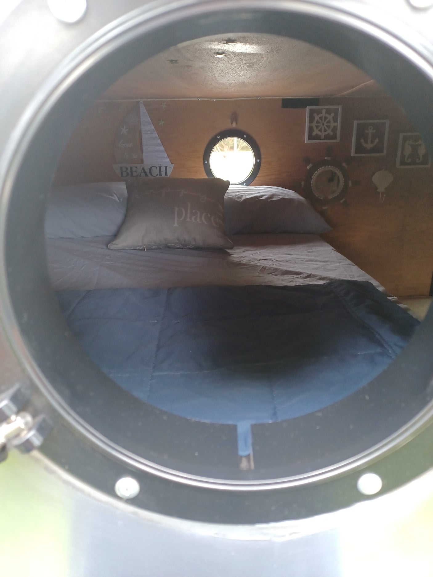 Inside a cozy RV rental, a nautical-themed bedroom features a porthole window and marine decor, viewed through a circular frame.