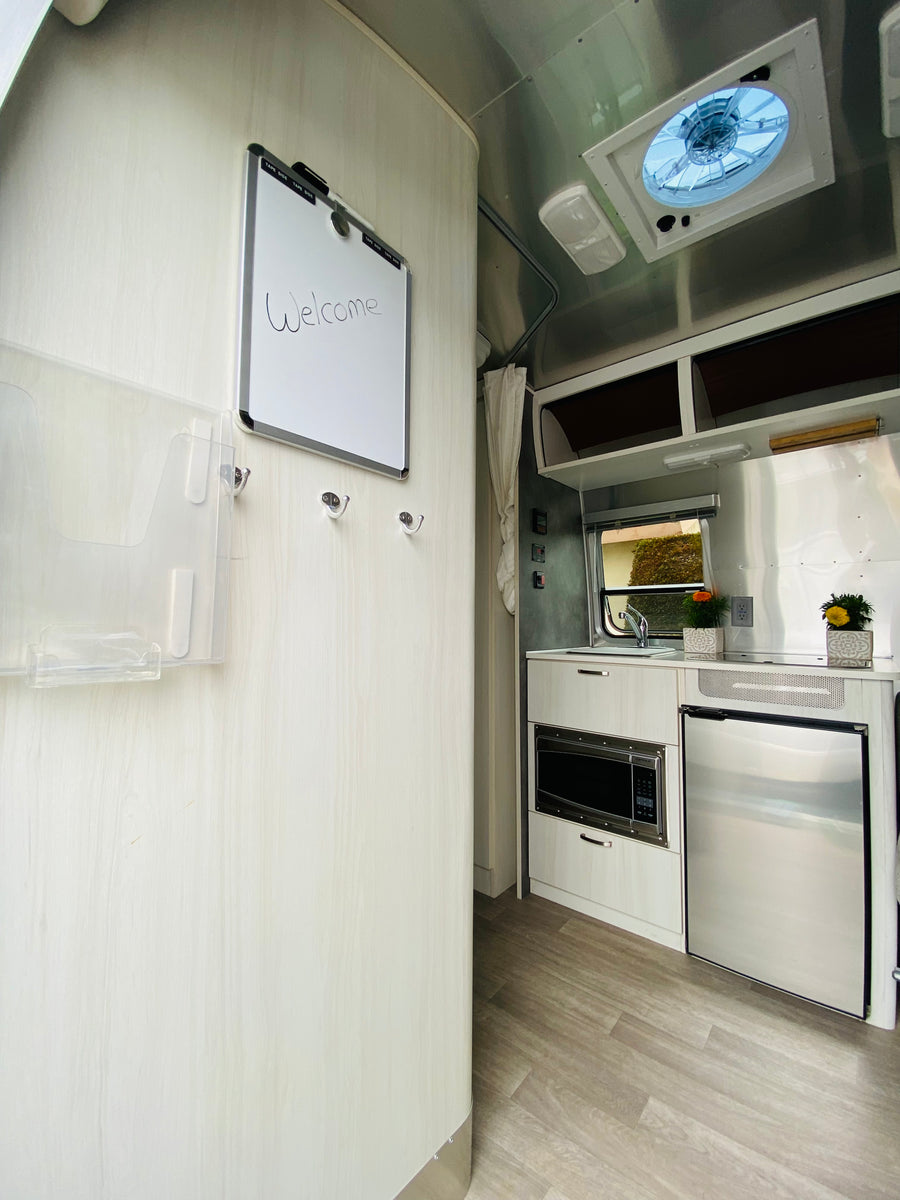 Welcome inside this RV rental, featuring a modern kitchen with microwave, fridge, and a handy welcome board.
