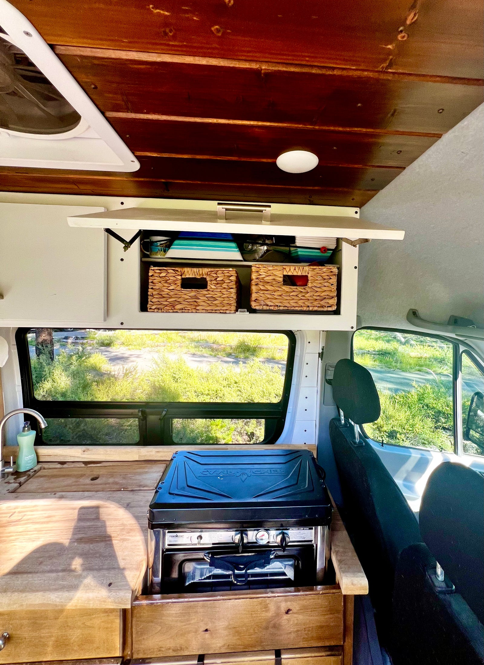 RV rental: Camper van interior with wood ceiling, overhead storage, sink, and a Camp Chef stove on the counter.