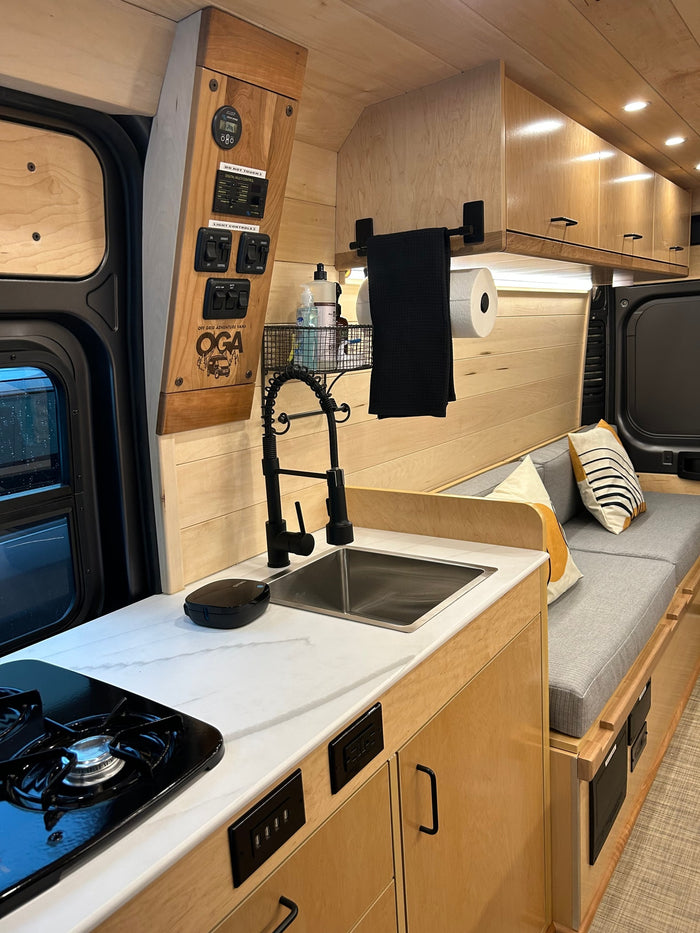 Modern RV rental interior: sleek kitchen with sink, stove, and cozy wood-paneled seating. Built for adventure.