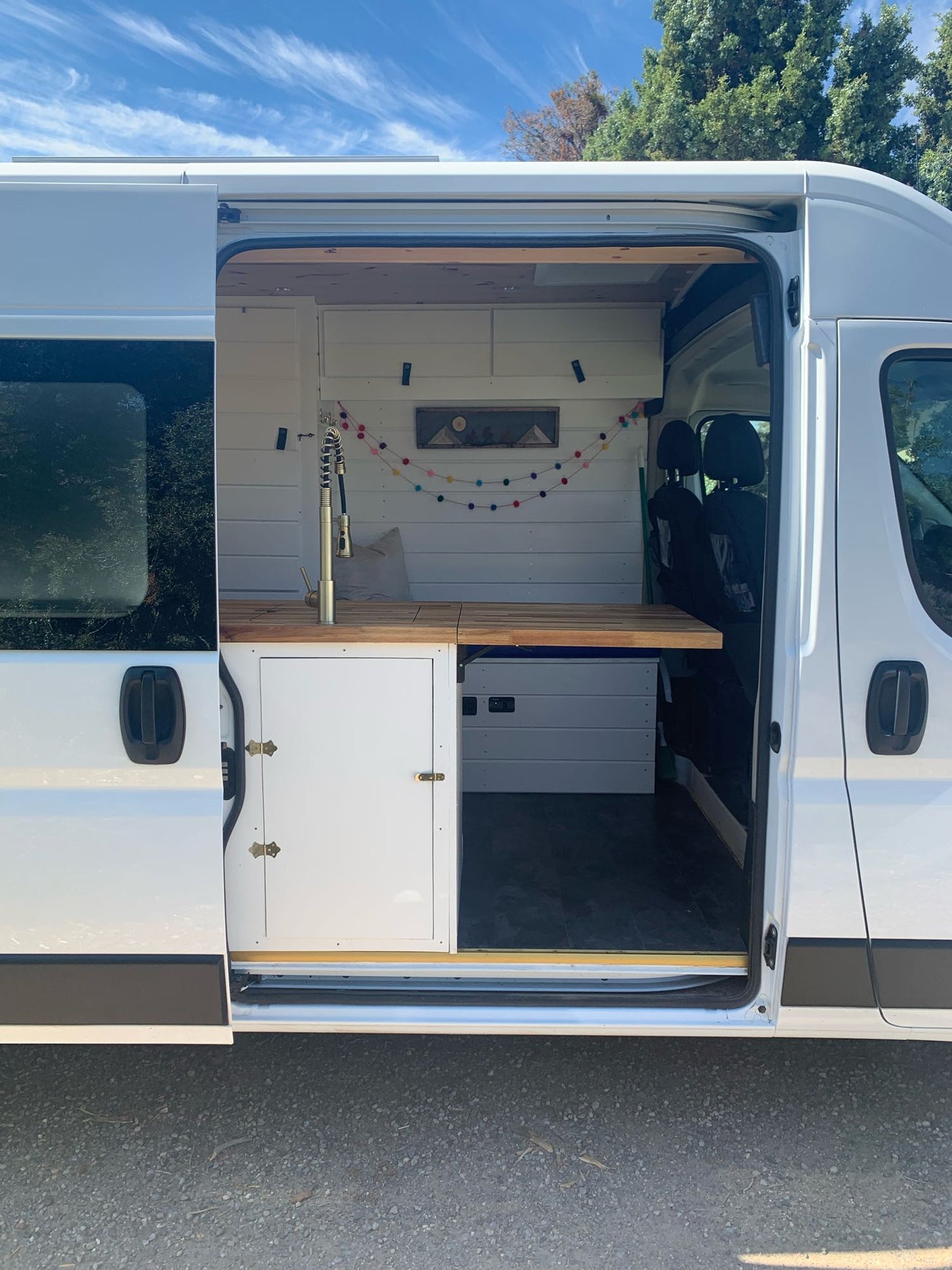 This white RV rental camper van showcases its cozy interior through the open side door, featuring a kitchen and bed.