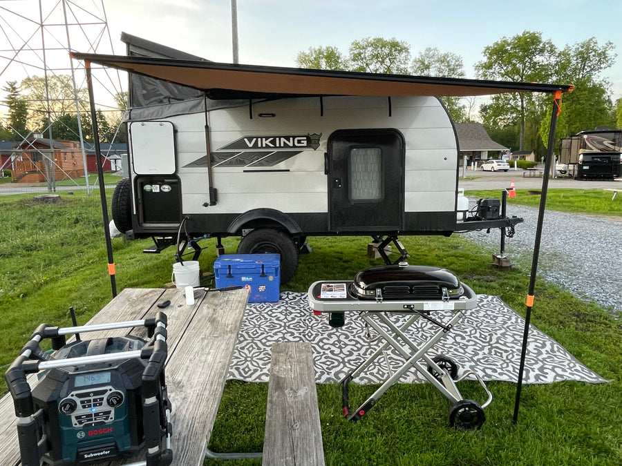 This RV rental showcases a compact Viking travel trailer with an extended awning, outdoor grill, and picnic table at a serene campground.