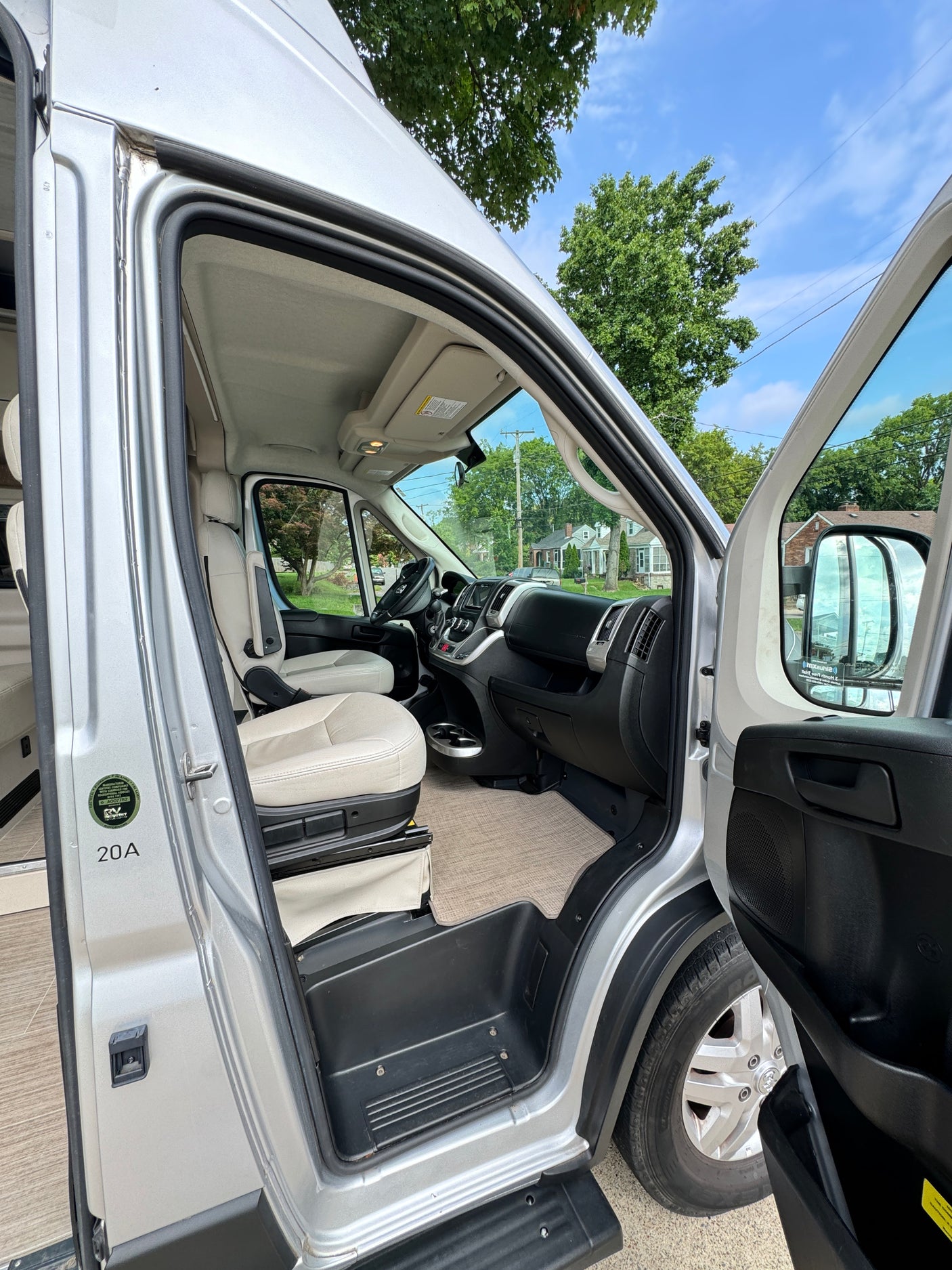 View inside an RV rental from the open passenger door, revealing the front cabin with light seats, dashboard, and a street scene outside.
