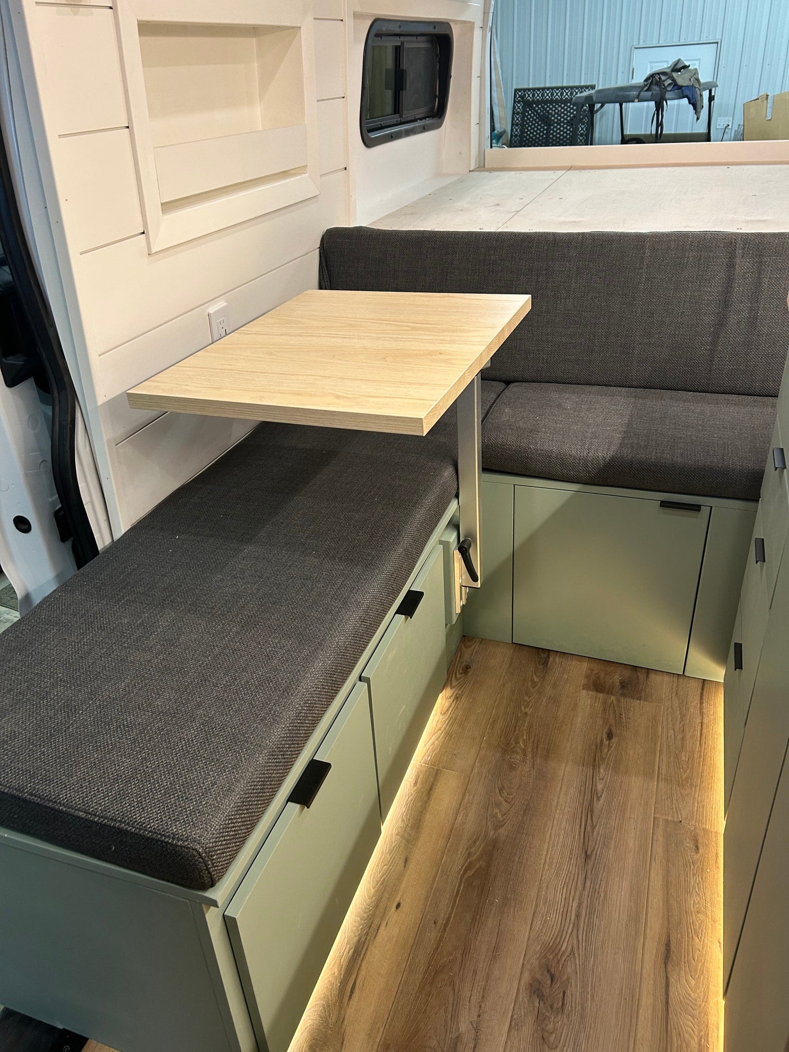 RV rental interior: modern dinette with wood table, gray cushions, sage green storage, and under-cabinet lighting.
