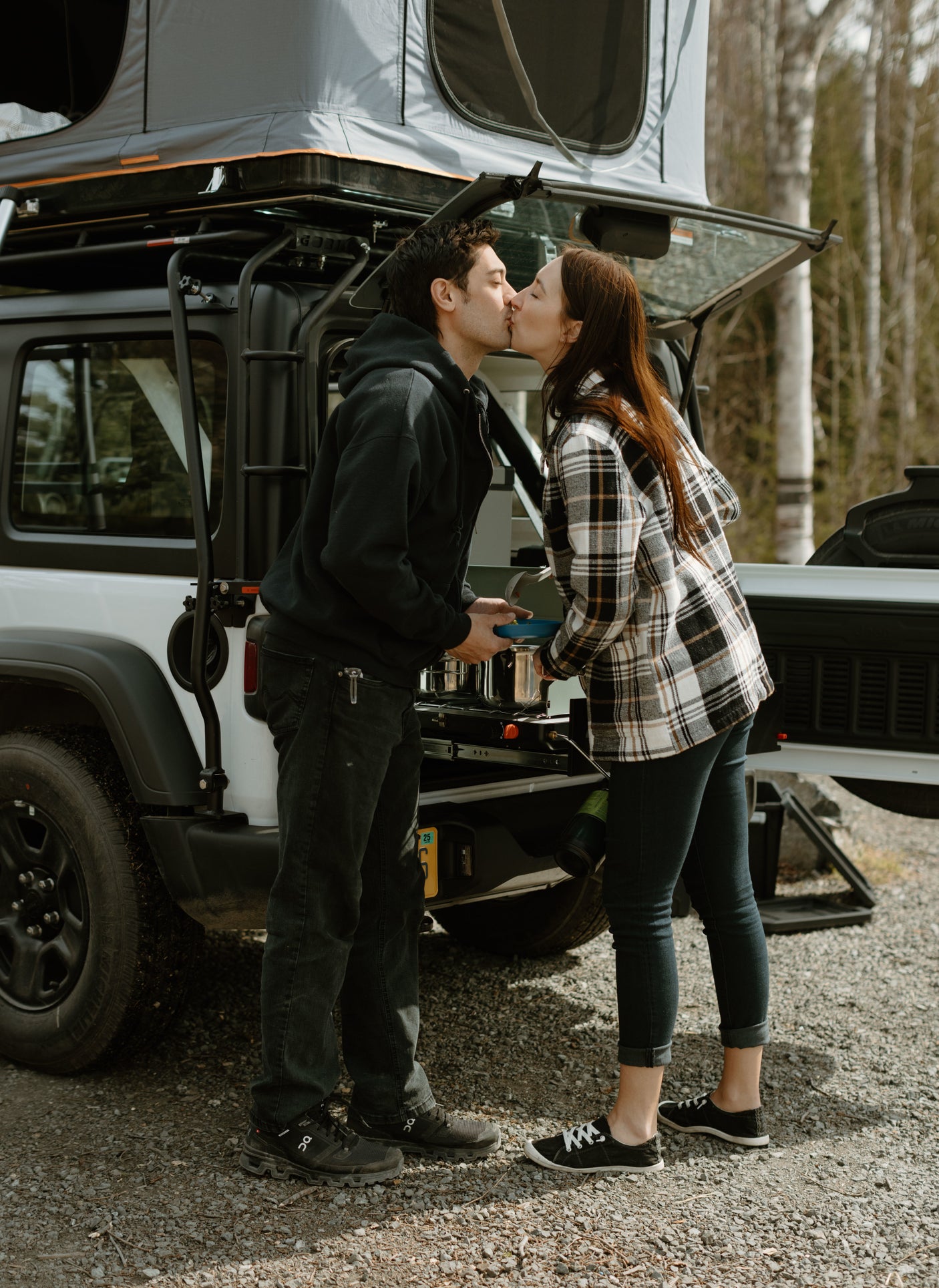 Couple shares a kiss by their RV rental, an SUV with a rooftop tent, ready for a camping adventure.