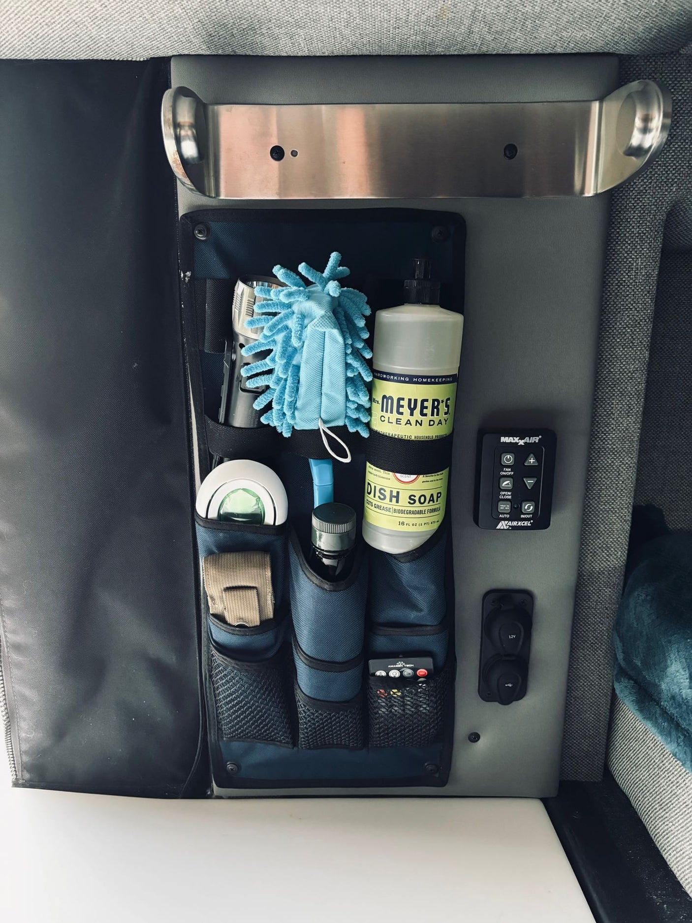 RV rental interior showing compact storage pockets, cleaning supplies, Maxxair fan control, and 12V outlet for easy access.