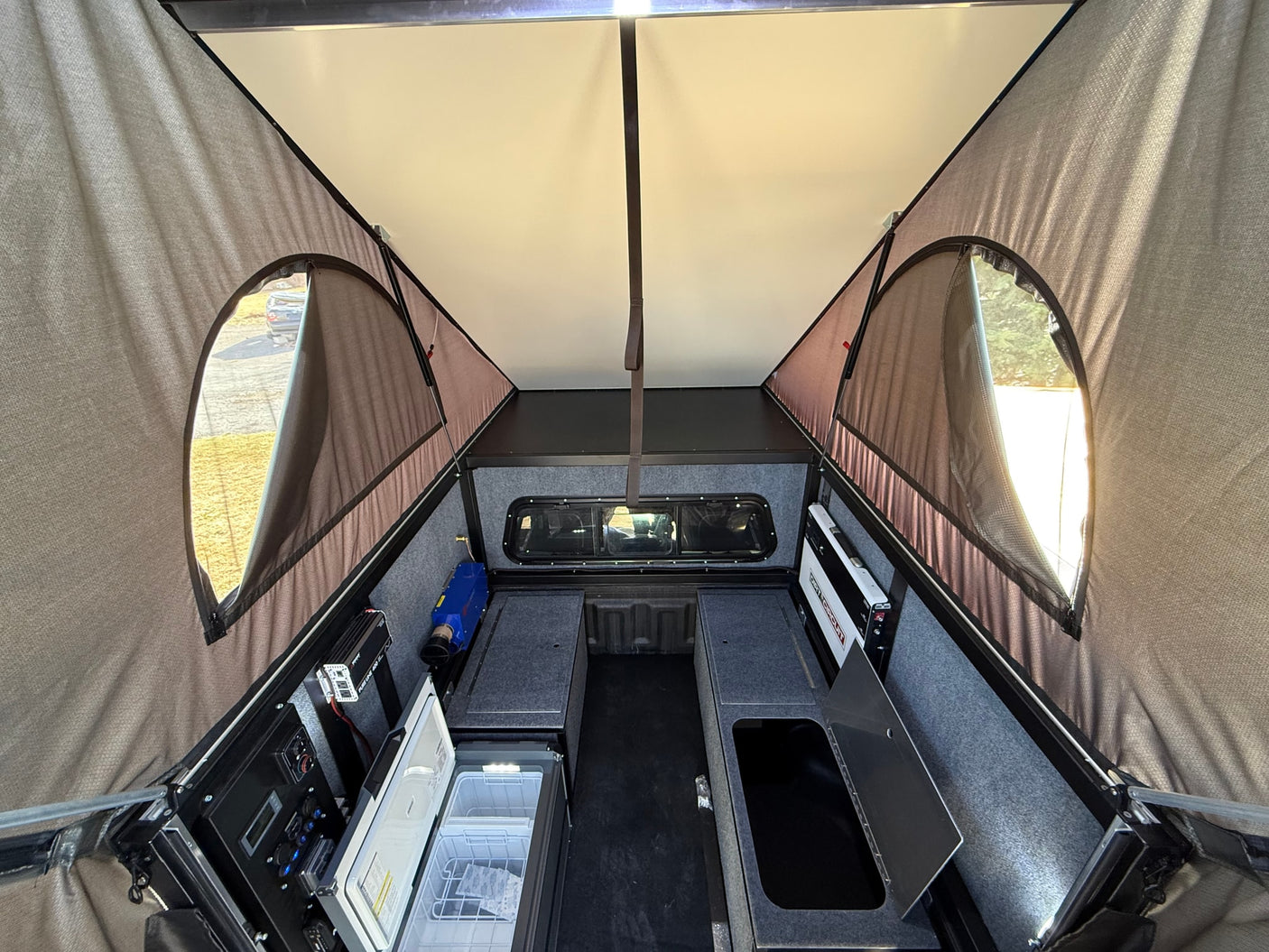 Inside a truck camper, ideal for RV rental, with a fridge, power panel, and pop-up tent for camping comfort.