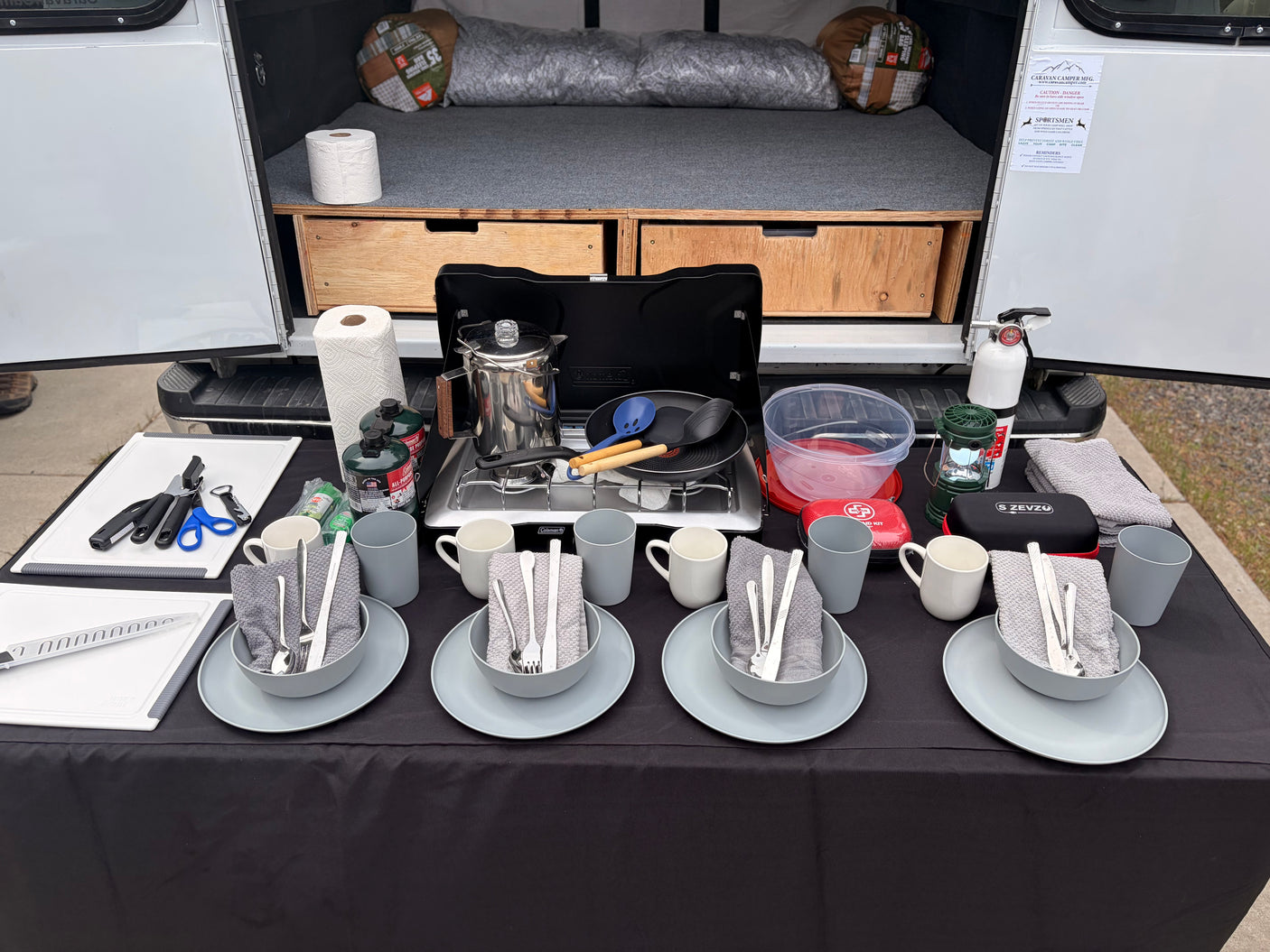 An RV rental's organized outdoor kitchen with a stove, coffee pot, cooking gear, and place settings for four.