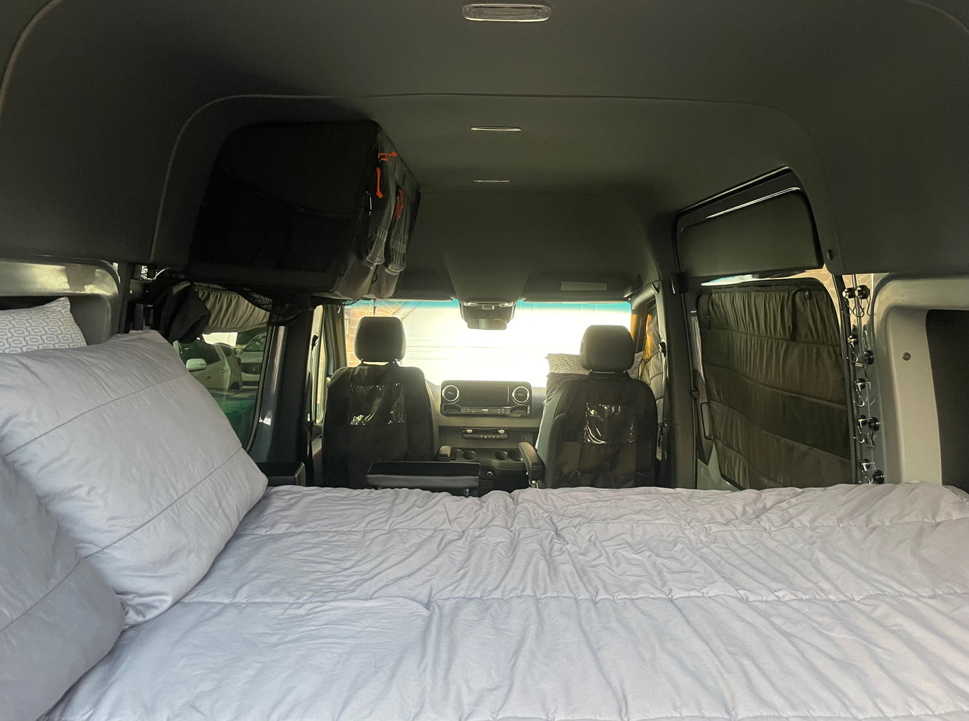 Inside an RV rental, a comfy bed fills the foreground, leading to the front cabin with seats and overhead storage.
