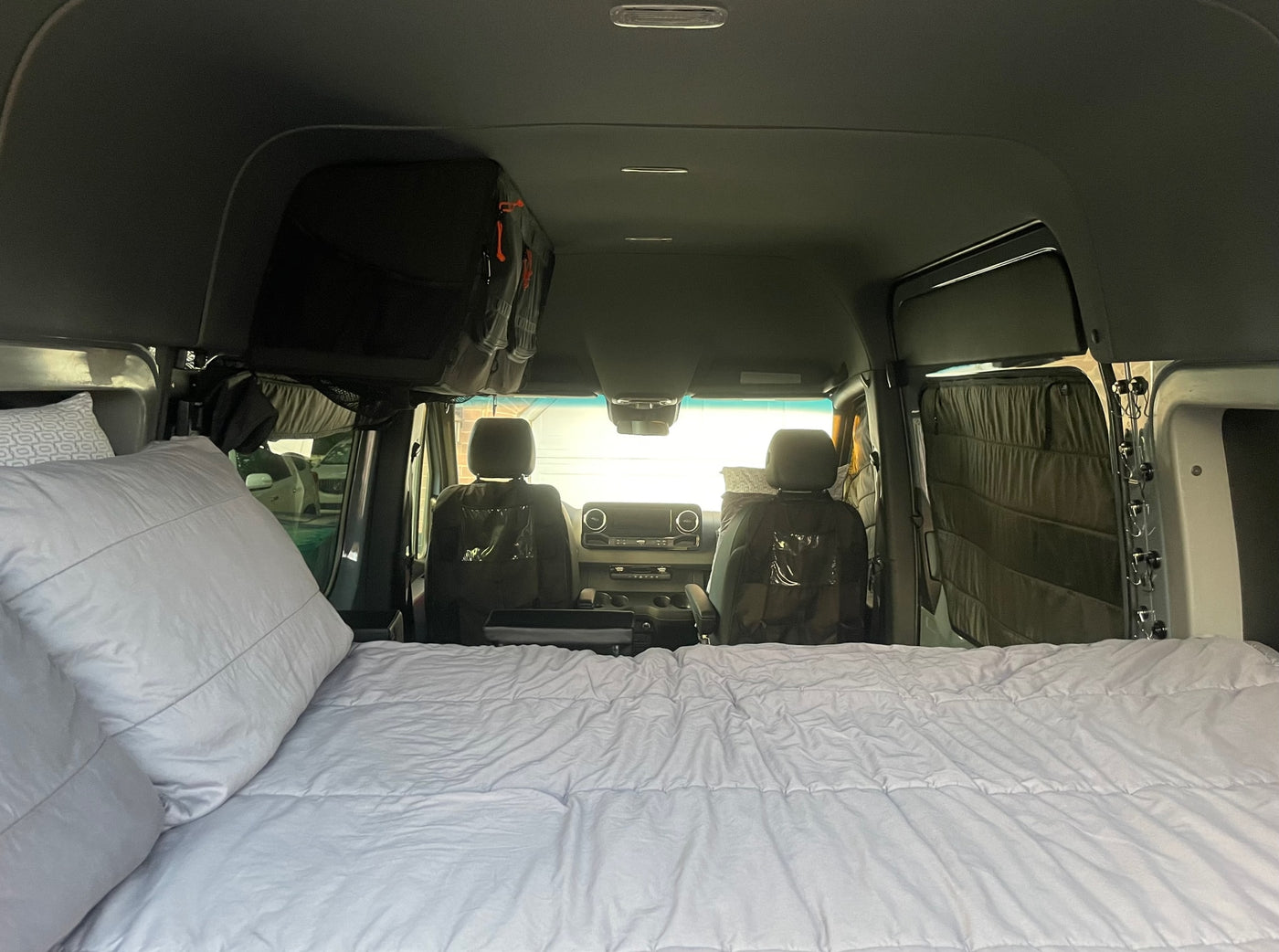 Inside an RV rental, a comfy bed fills the foreground, leading to the front cabin with seats and overhead storage. — photo 14
