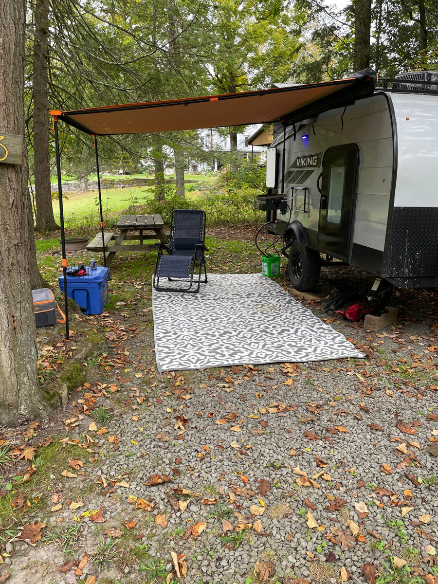 Relaxing rv rental campsite with a small travel trailer, extended awning, outdoor rug, chair, cooler, and picnic table.