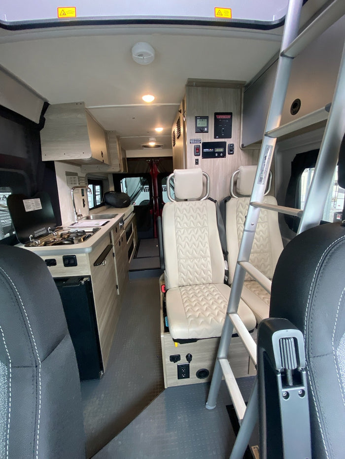 Interior of an RV rental, featuring a compact kitchenette, ladder to bunk, and comfortable seating. Ready for adventures!