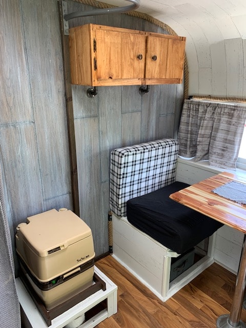 RV rental interior: A wooden cabinet, cozy dinette with plaid cushion and table, plus a portable toilet, all in a compact space.