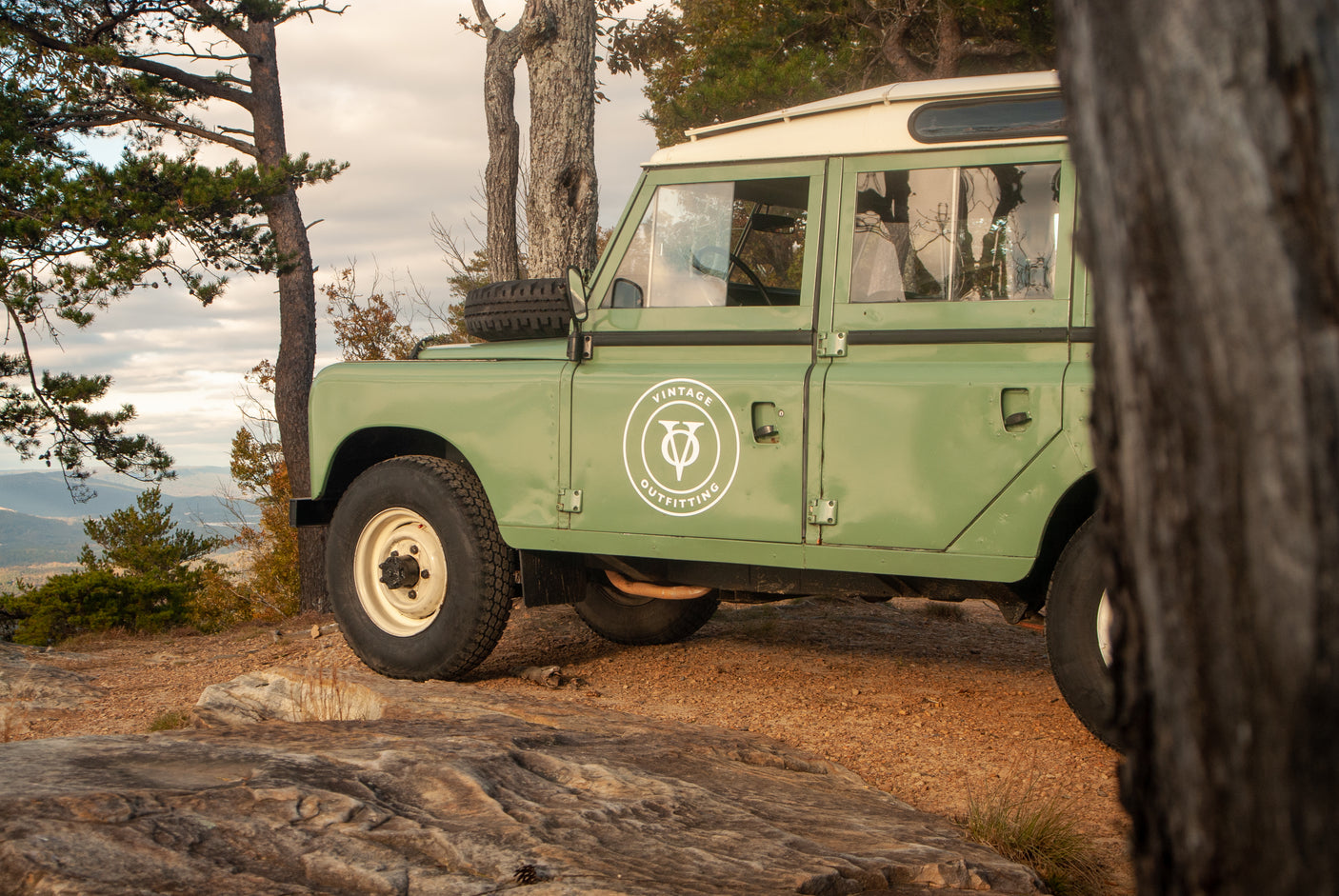 A vintage green Land Rover sits on a mountain lookout. Experience similar outdoor adventures with our RV rental service.