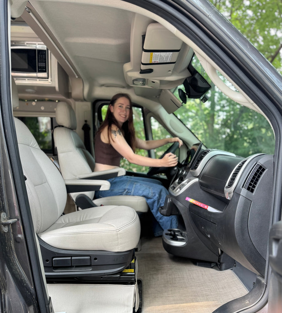 This RV rental's cozy interior features a smiling woman in the driver's seat, ready for a road trip adventure.