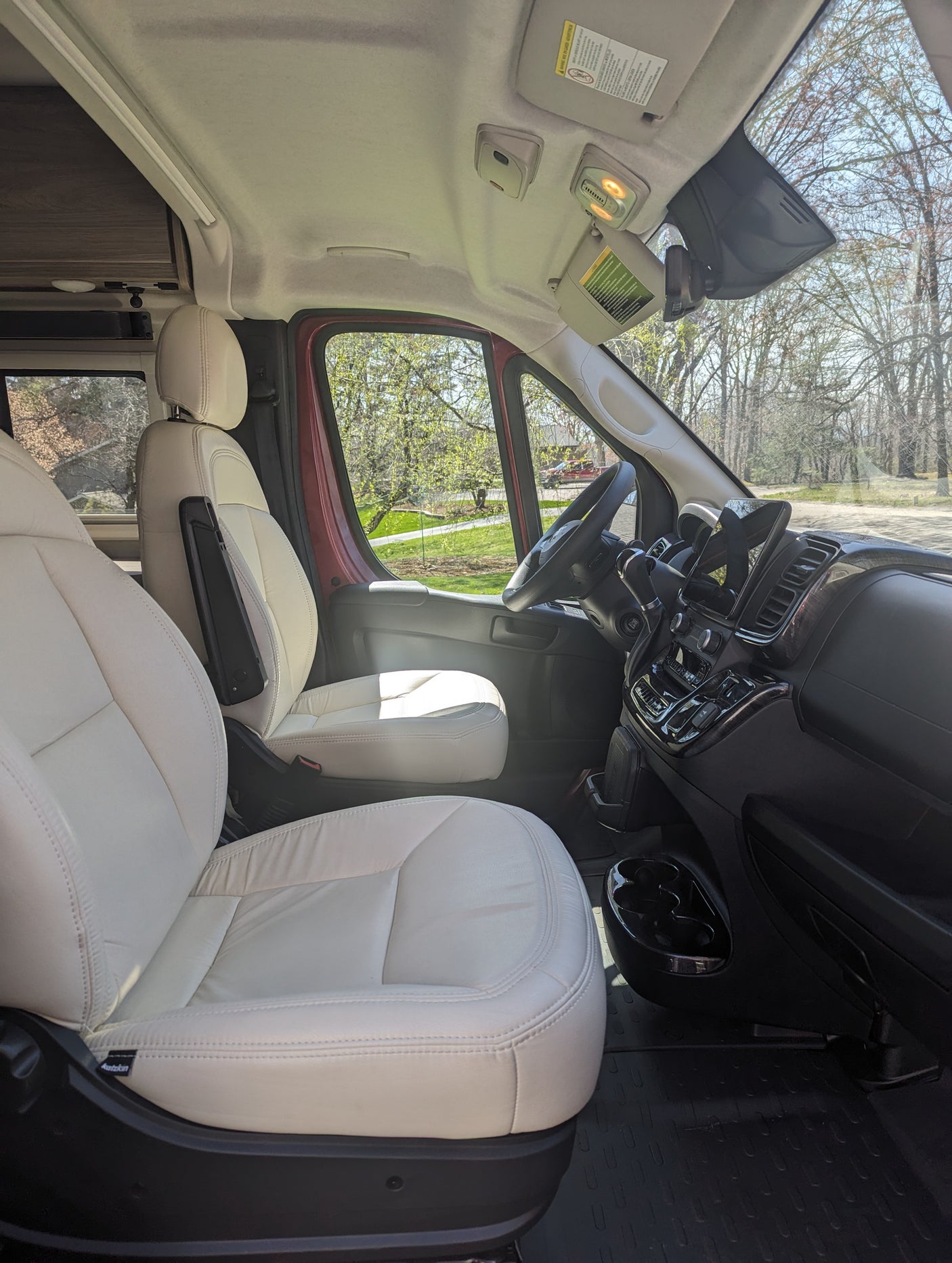 Spacious, light-colored leather interior of a modern camper van, perfect for an RV rental adventure. Shows front seats & dashboard.