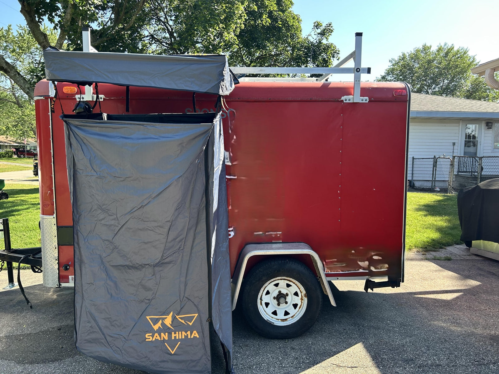 Red cargo trailer converted for RV rental use, featuring a deployable privacy tent and roof rack.