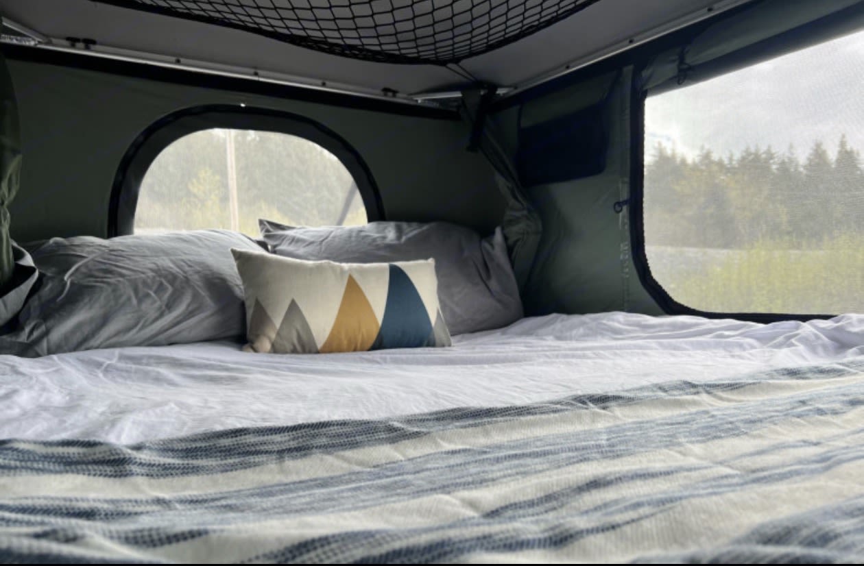 on a beach by the ocean and mountains. Perfect for adventure!|Adventure-ready dark green pickup with a Thule Tepui rooftop tent and ladder