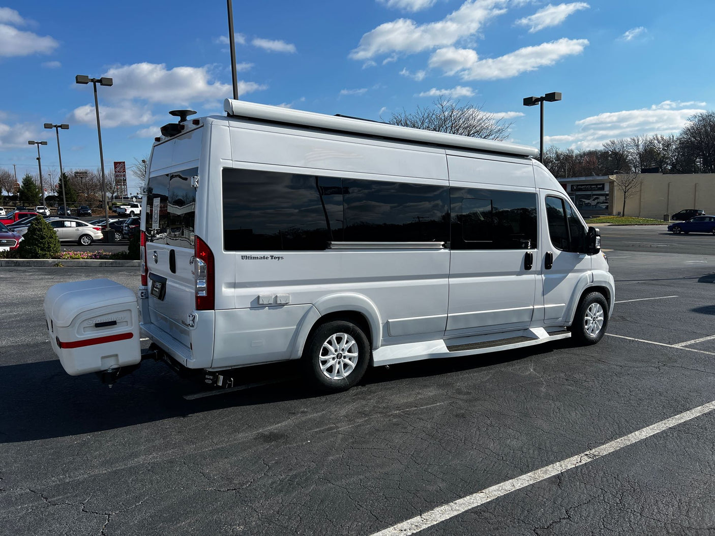 Ultimate Toys RV rental: A white camper van with an awning and rear storage box, parked in a bright outdoor lot.
