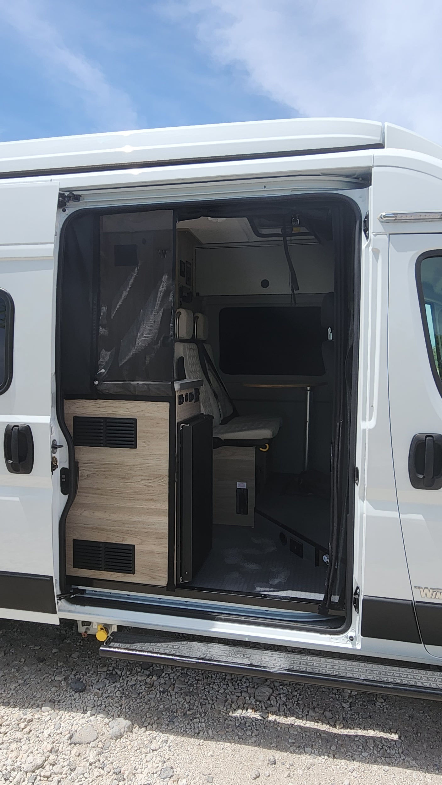 Inside an RV rental: a white camper van's interior, showcasing a compact kitchen & bed area. Perfect for van life.