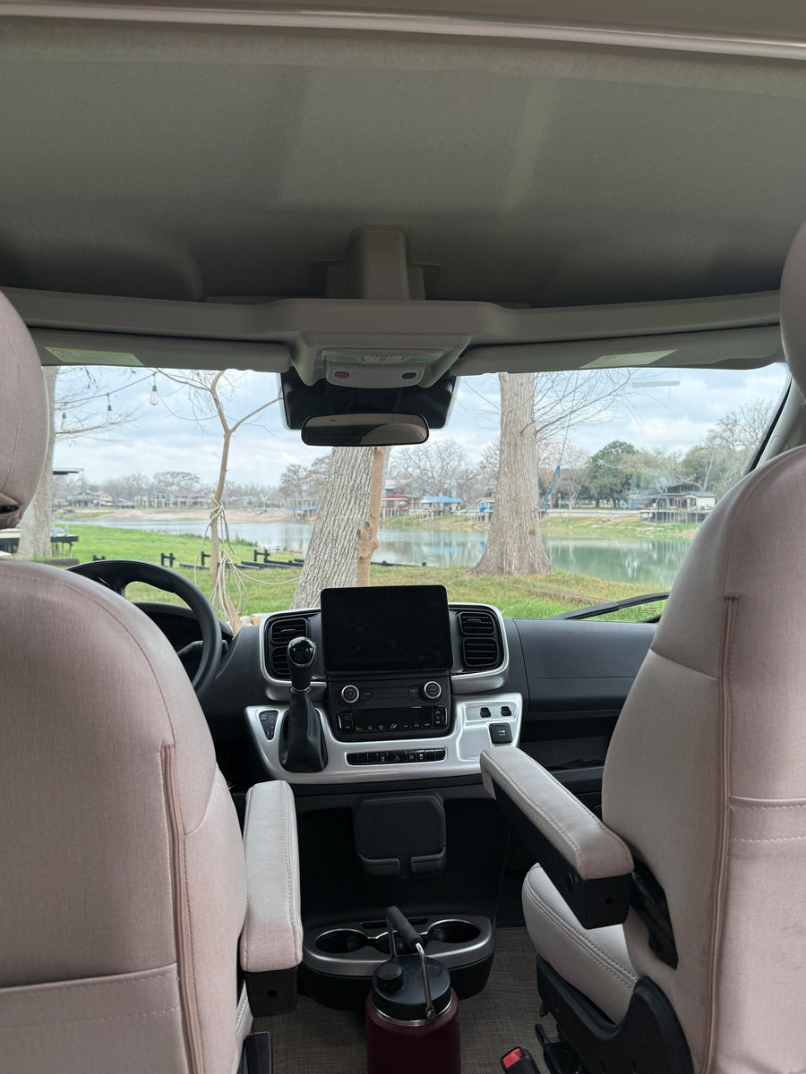 RV rental interior: dashboard, comfortable seats, and a large water bottle, with a serene lake view through the windshield.