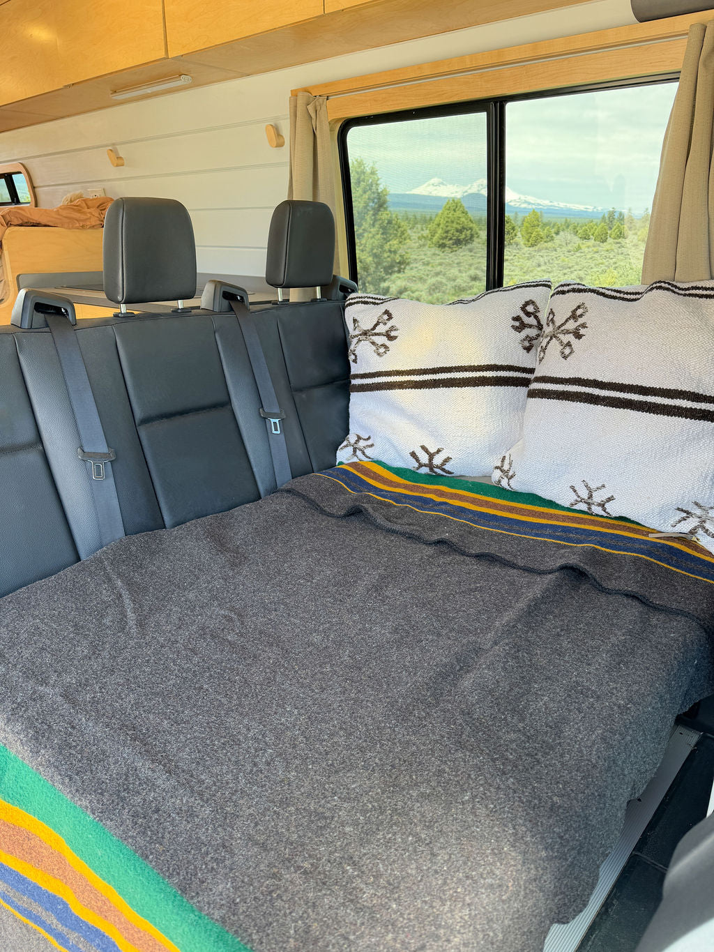 Cozy RV rental interior featuring a comfortable bed setup on converted seats, with stunning mountain views outside the window.
