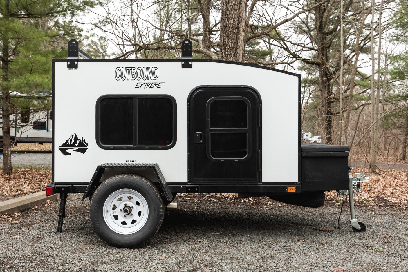 Compact white Outbound Extreme camper trailer, ideal for an RV rental adventure, parked on gravel with trees.