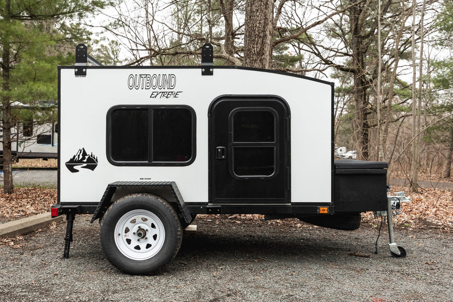 Compact white Outbound Extreme camper trailer, ideal for an RV rental adventure, parked on gravel with trees.