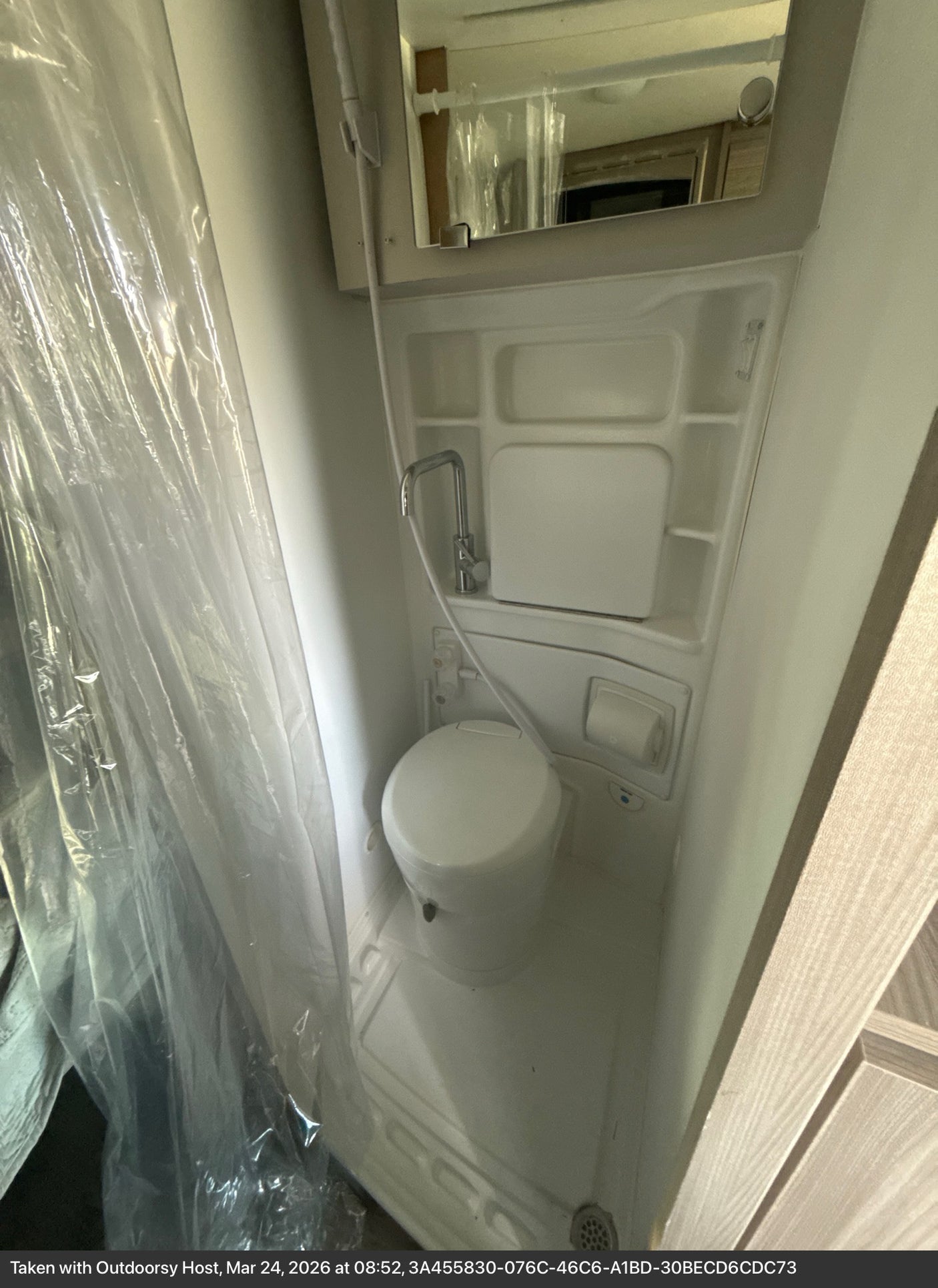 This rv rental features a compact bathroom with a toilet, shower, plastic curtain, and mirror, perfect for small spaces.