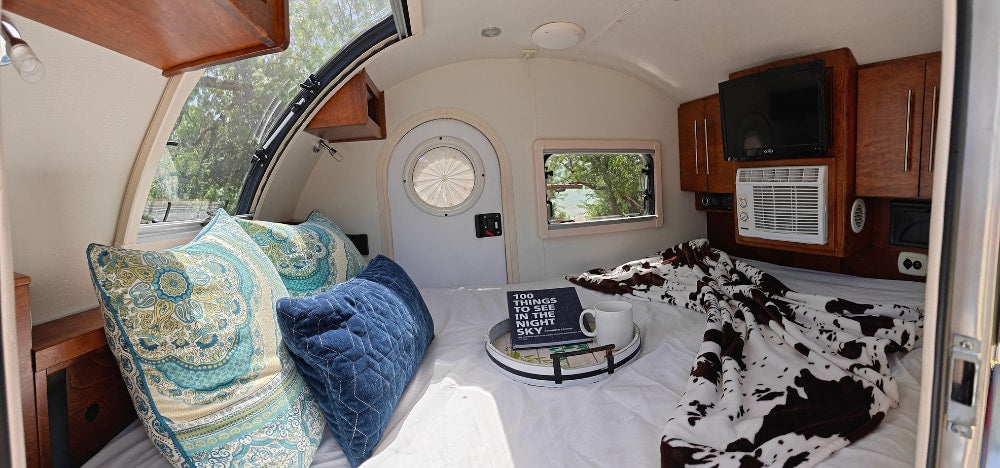 nestled in a shaded camp spot under trees.|Cozy rv rental: a compact interior with a bed — photo 1
