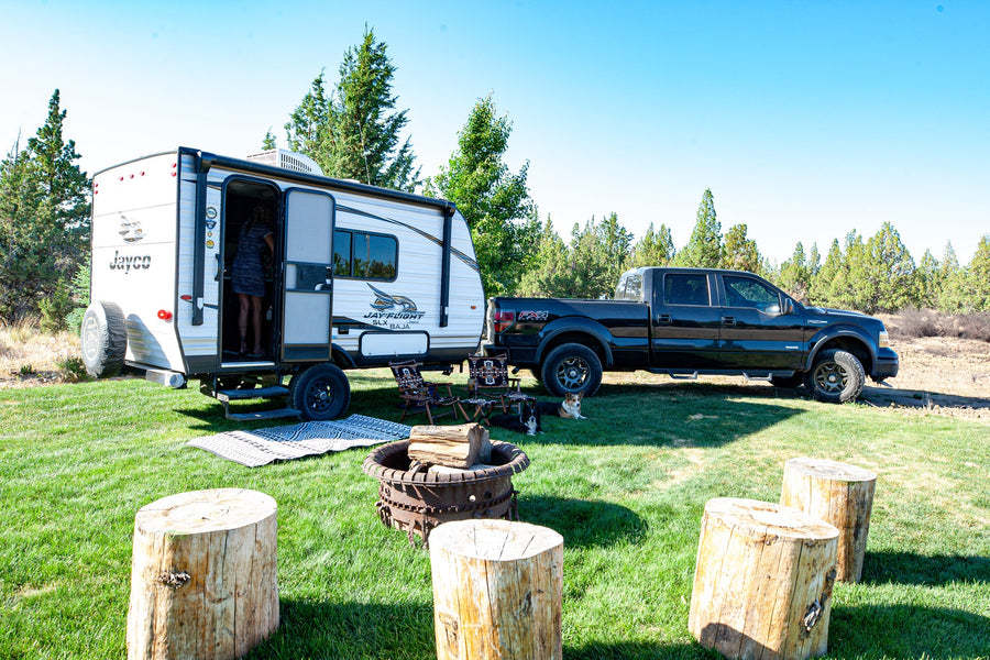 An RV rental travel trailer and truck are set up at a sunny campsite. A woman is in the doorway