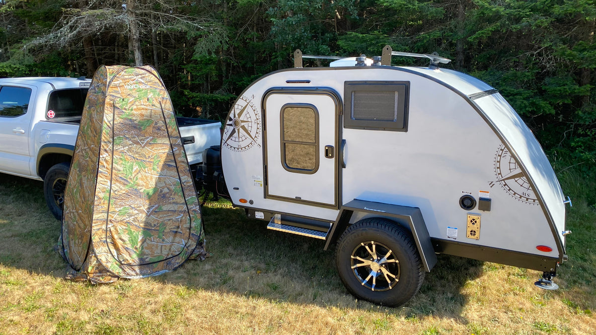 RV rental ready: A light grey teardrop camper and camouflage privacy tent beside a white truck in a sunny, grassy area. — photo 6