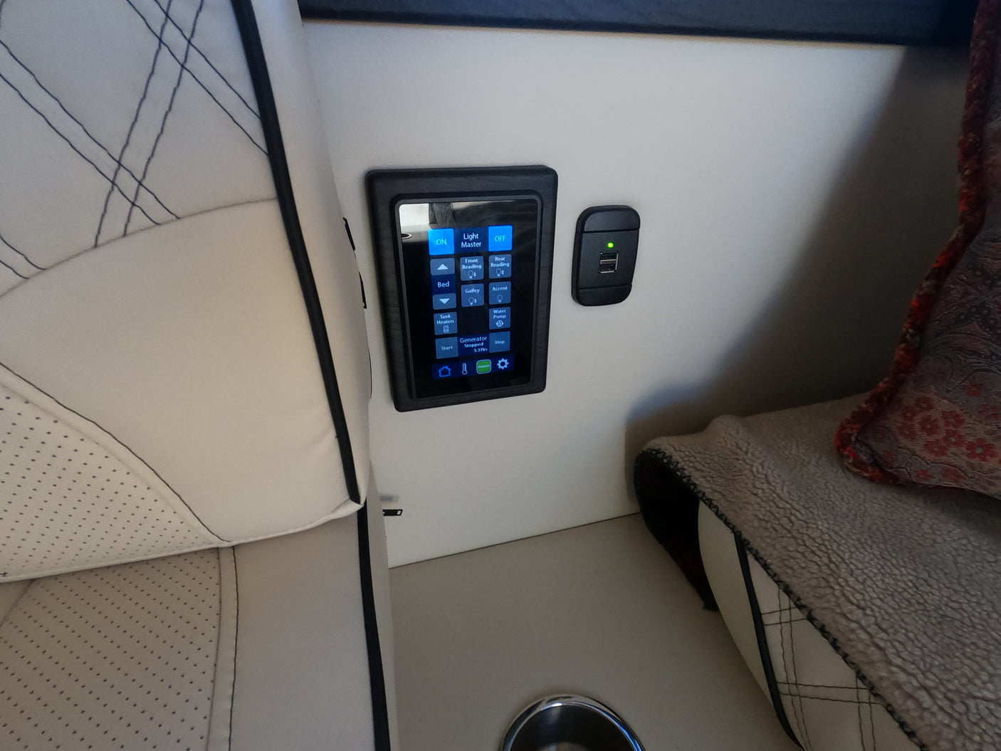 RV rental interior showcasing a touchscreen control panel for lighting/utilities and a USB charging port beside comfortable, quilted seating.