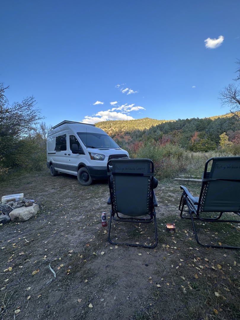 Enjoying a scenic RV rental camping trip with a camper van, chairs, and a fire pit under a clear blue sky.