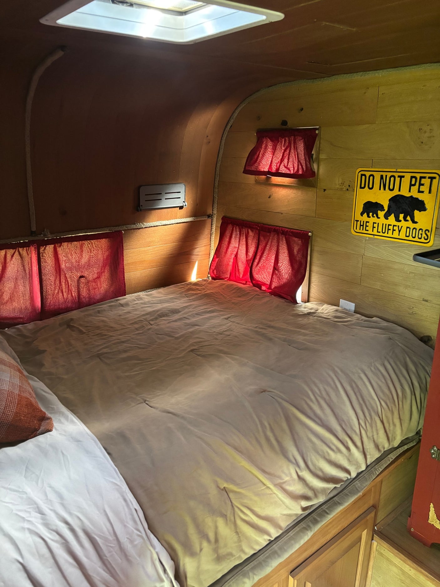 set outdoors among tall trees under a blue sky.|Outdoor grilling by a colorful vintage camper. This RV rental offers a cozy setup for your next camping adventure.|Cozy RV rental interior features a comfortable bed