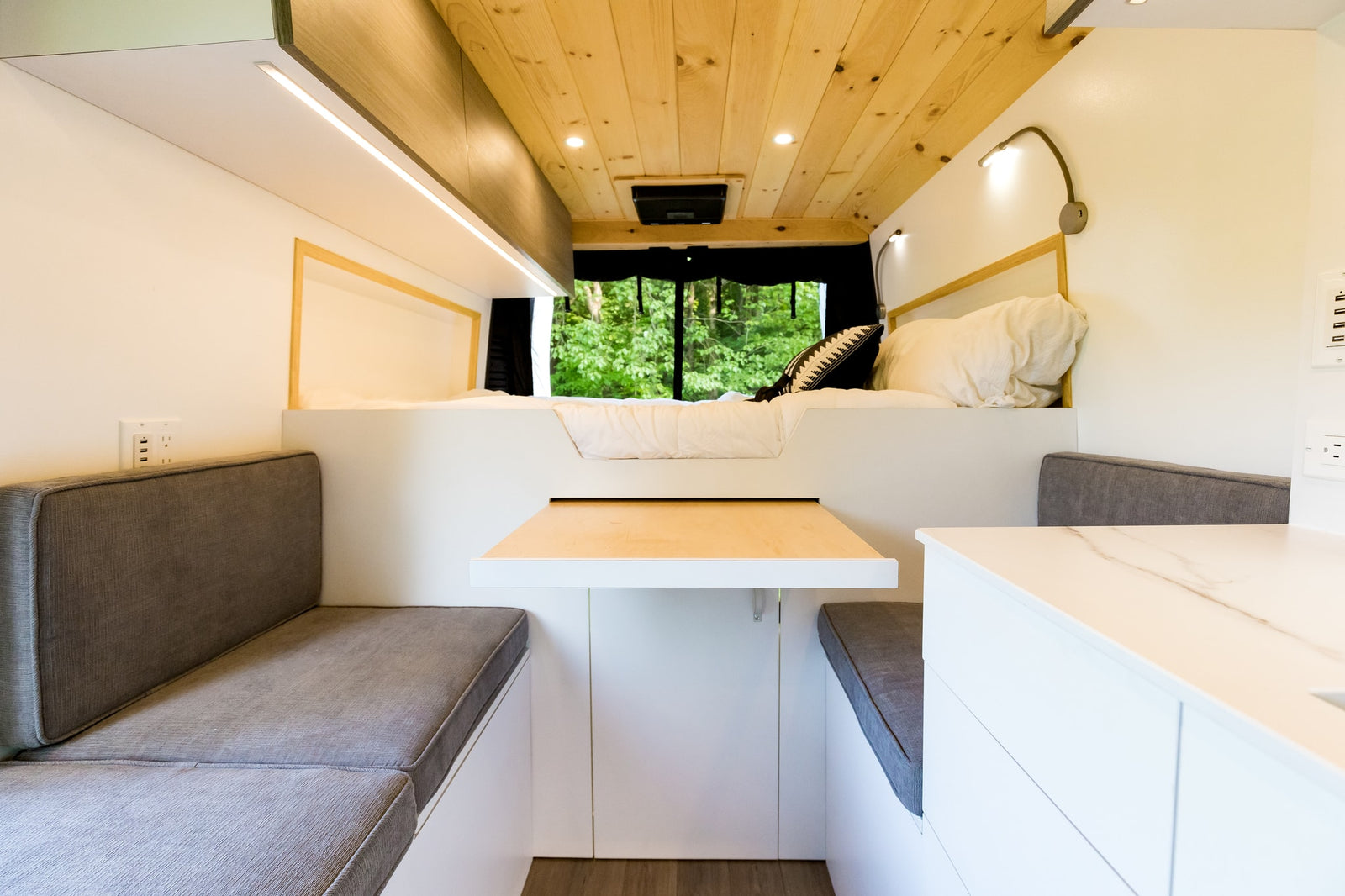 Stylish RV rental interior with a comfy bed, flexible dinette & table, ambient lighting, and a window framing nature.