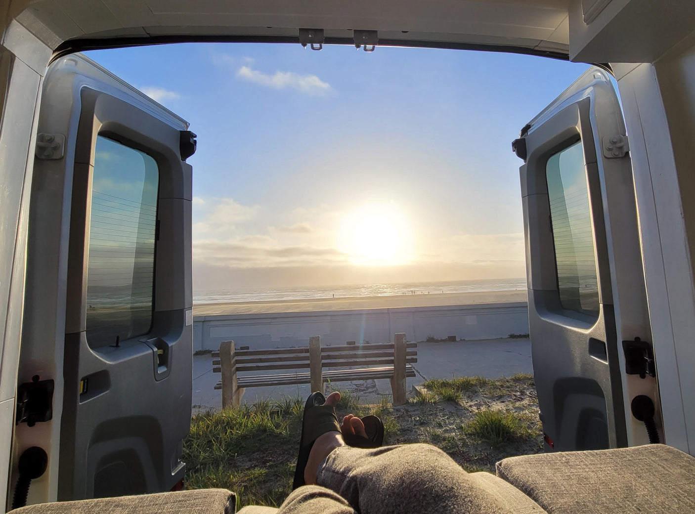 Enjoying the beach sunset from an RV rental. Open doors offer a relaxing view of the ocean, sand, and bench from inside the camper.