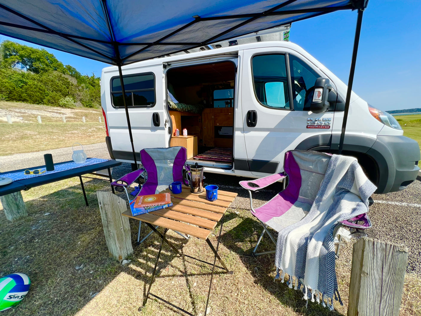 RV rental parked with a shaded outdoor setup, featuring chairs, coffee, books, and a blanket for relaxation.