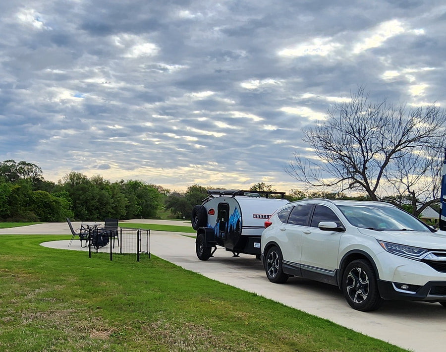 parked at an RV site. Ideal for an RV rental outdoor adventure.|White SUV towing a sleek RV rental teardrop trailer in a paved campsite with a patio and grass