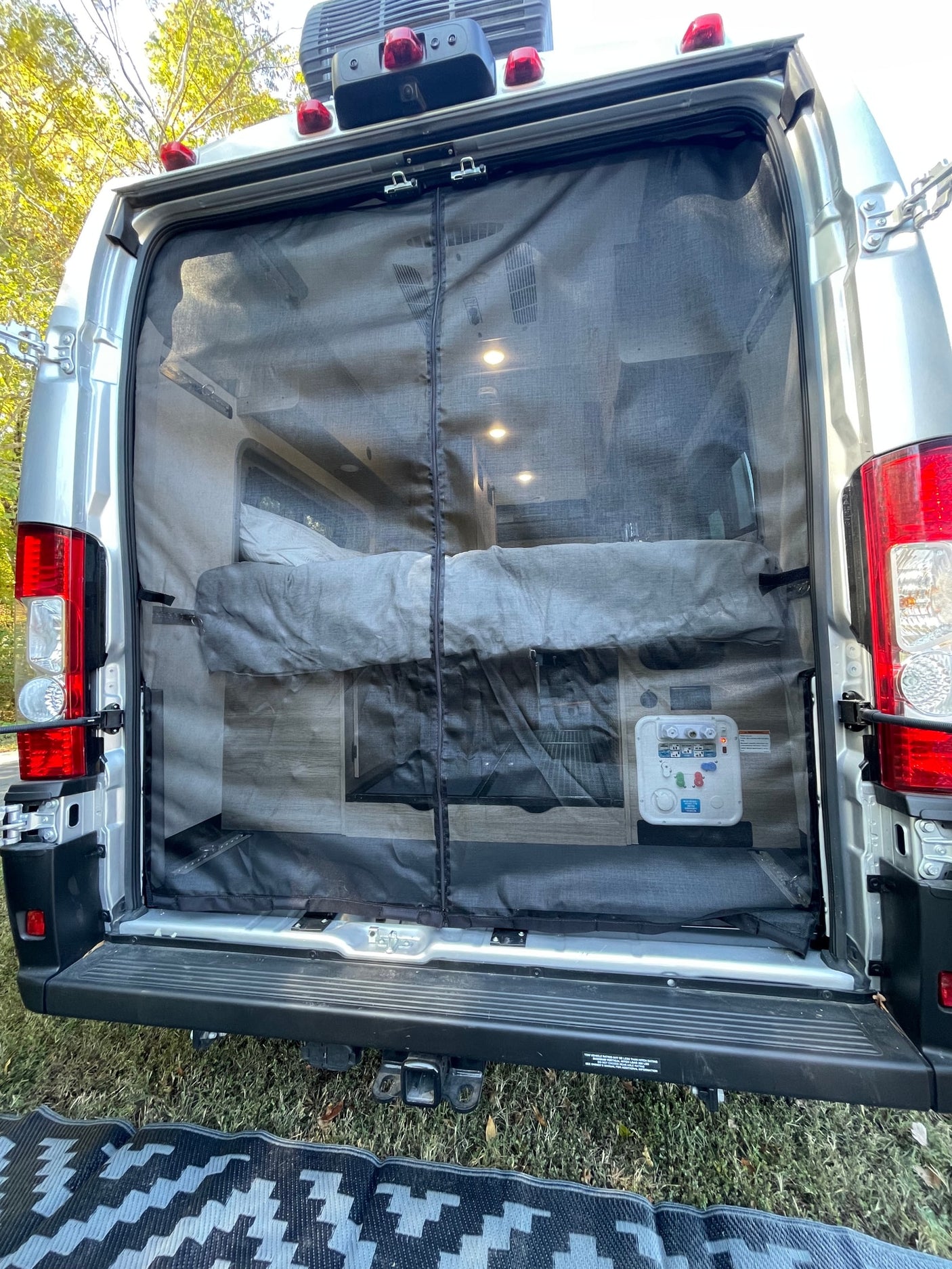 Rear view of an RV rental, doors open with a mesh screen, showing a cozy bed and interior lights, perfect for camping.