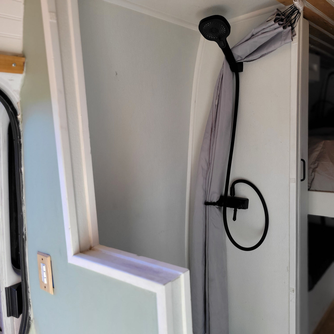 RV rental interior: A compact shower area with a modern black shower head, gray curtain, and light switch on wall.