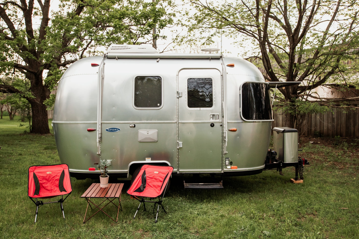Experience glamping with this Airstream RV rental! A shiny silver travel trailer with red camping chairs awaits your outdoor adventure.
