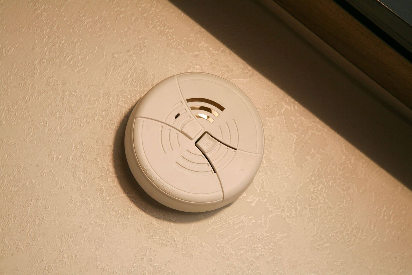 White smoke detector on a textured wall, essential for safety inside your RV rental.