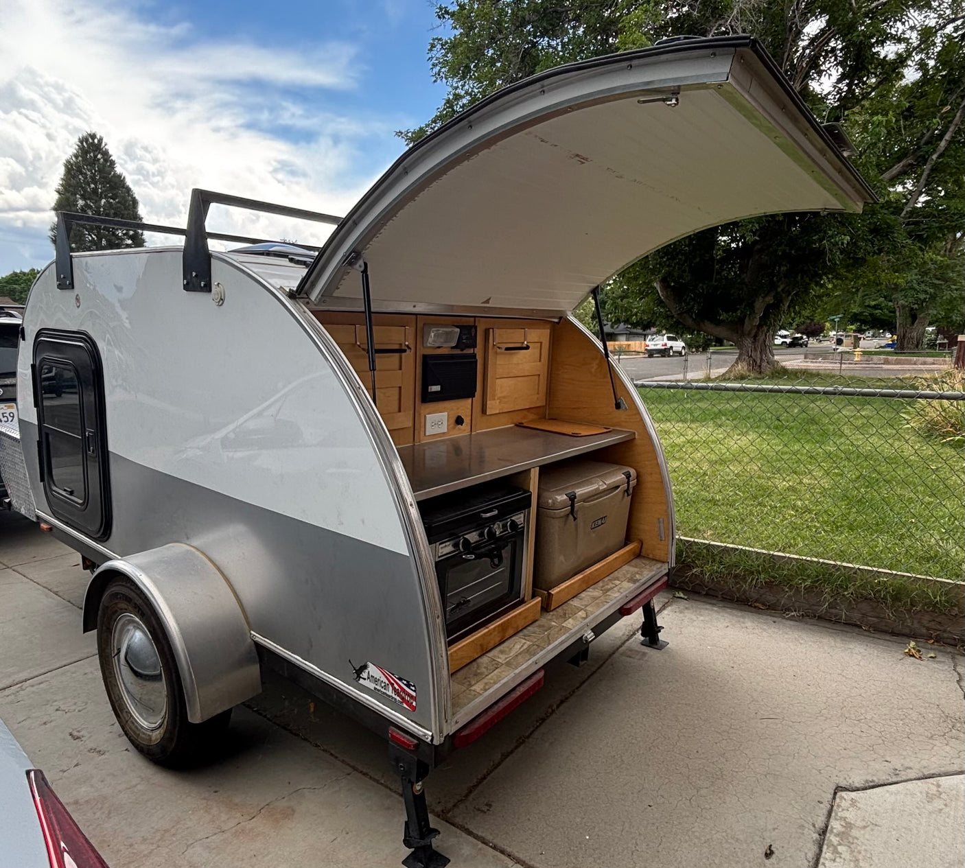 RV rental teardrop trailer features an open rear galley kitchen with stove, counter, cooler, and wood storage.