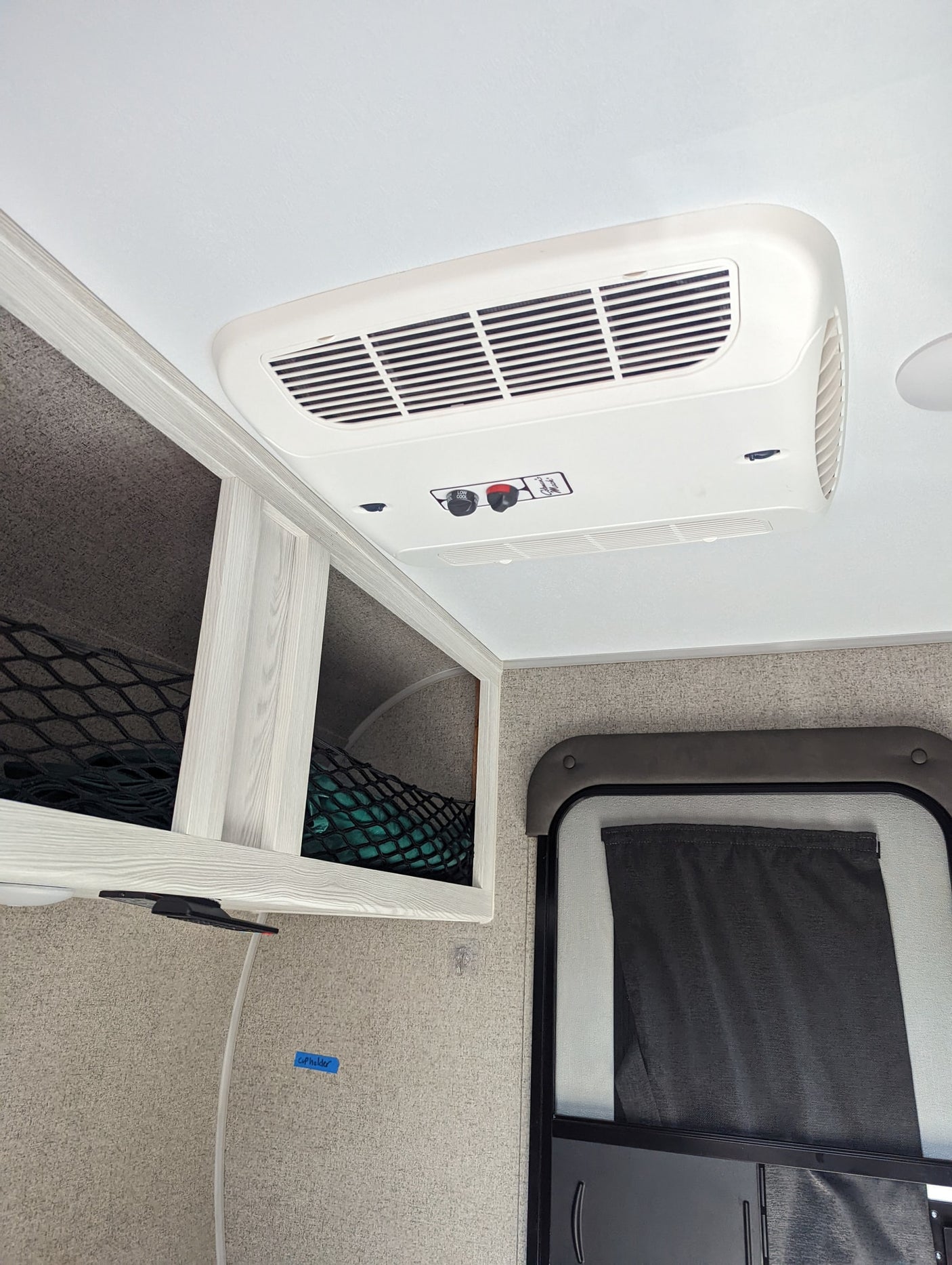 RV rental interior featuring a ceiling-mounted AC unit, overhead storage with nets, and a door with a pulled-down curtain.