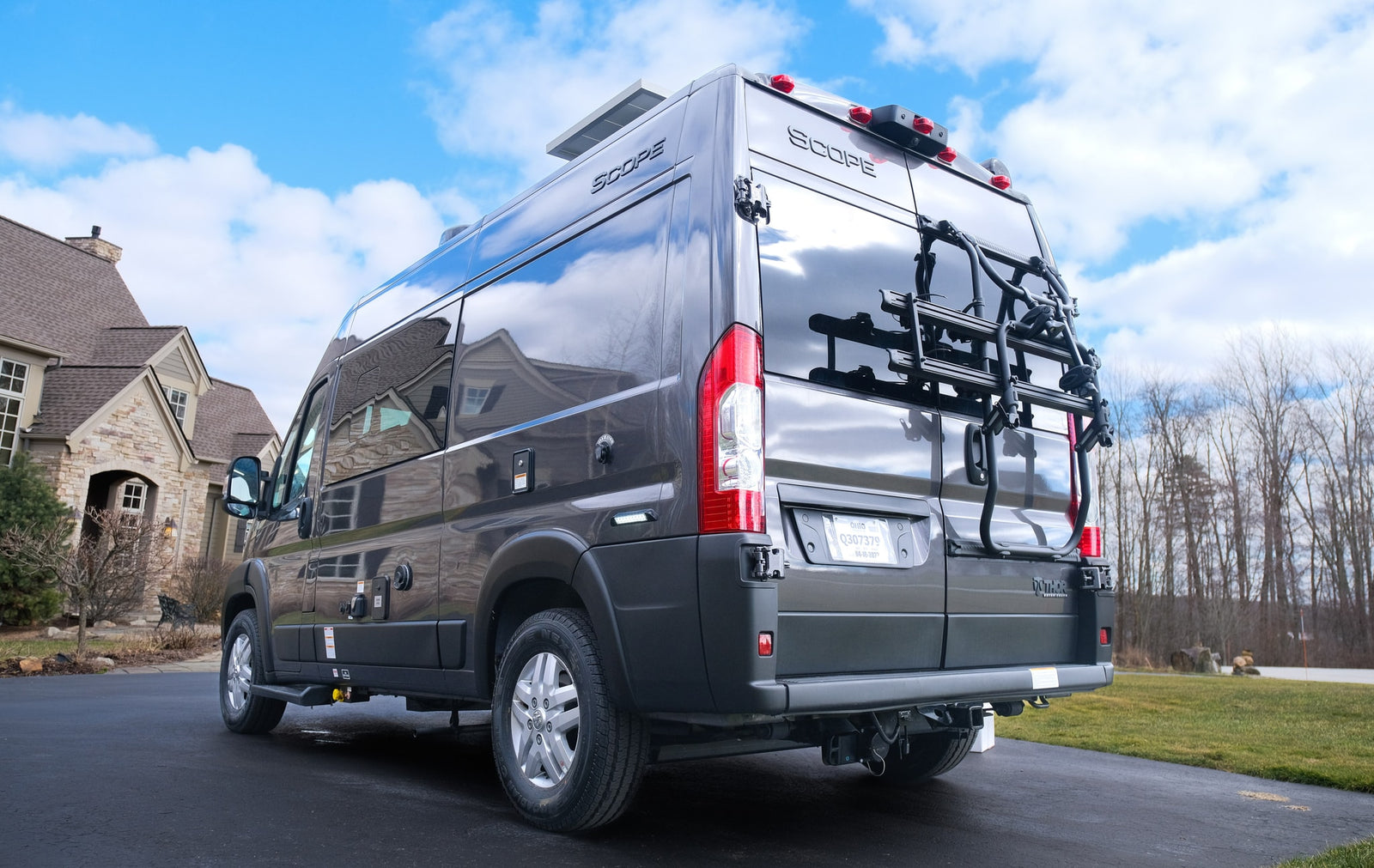 A dark gray Scope camper van, ideal for RV rental adventures, is parked in a driveway with a bike rack.