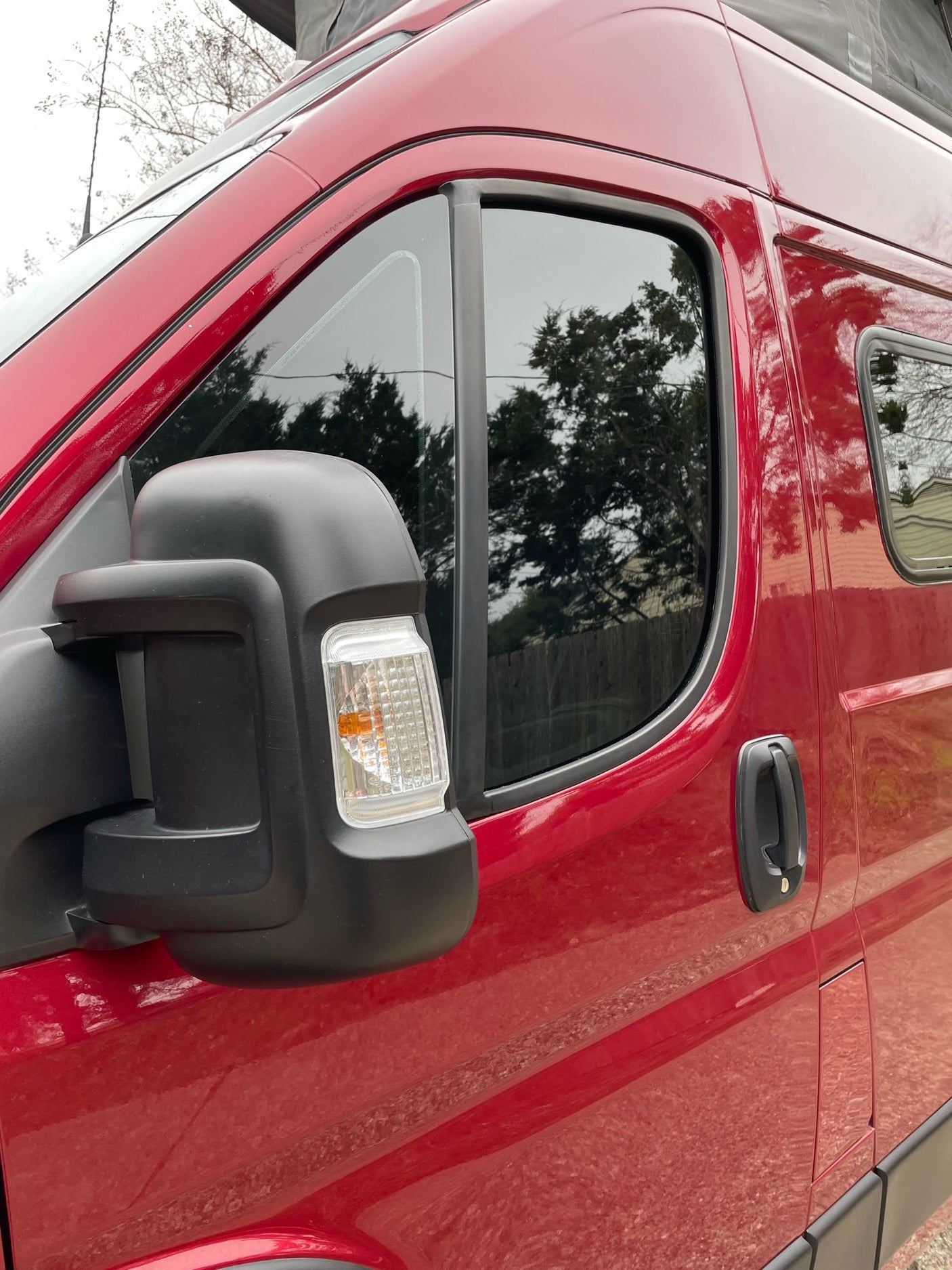 Red rv rental van exterior, featuring the driver's side door, tinted window, and a black side mirror with a turn signal.