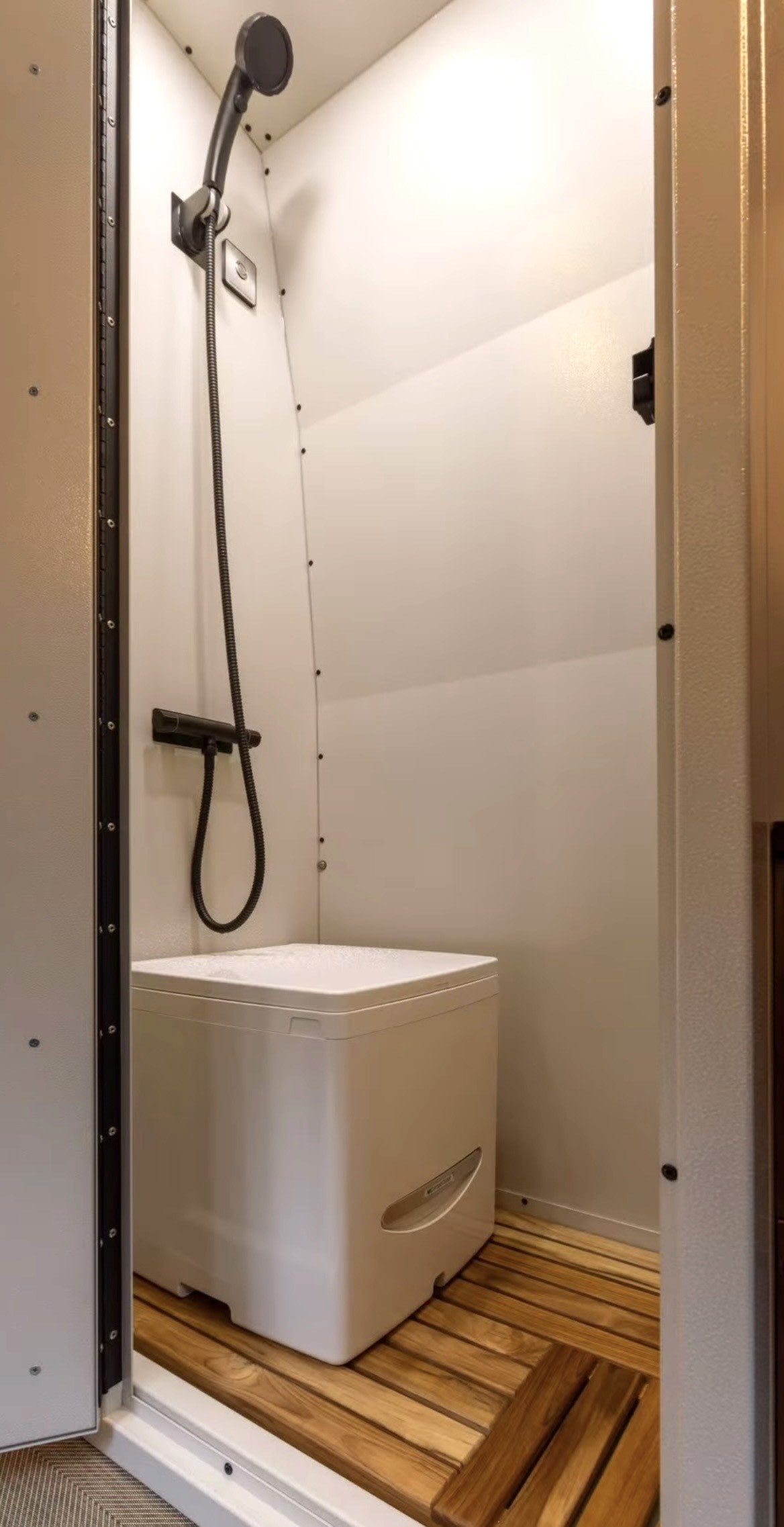 RV rental wet bath: compact shower with handheld head, modern toilet, and slatted wood floor for a convenient mobile bathroom.